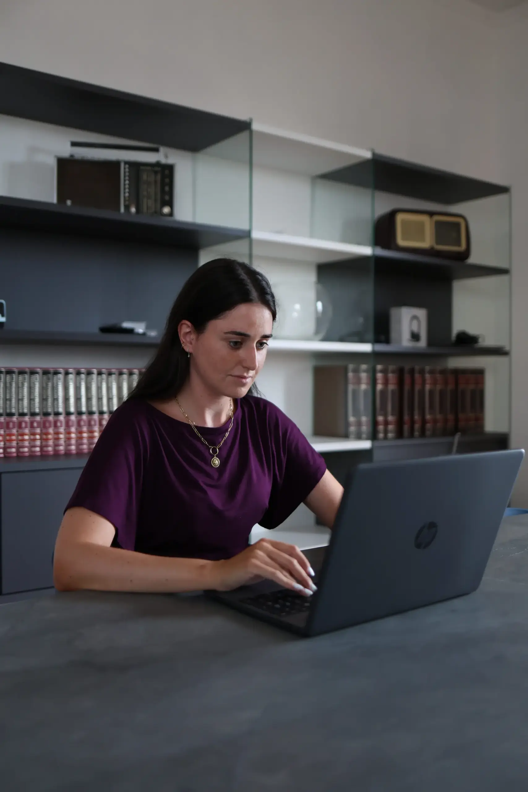 Una professionista aziendale concentrata mentre lavora al proprio computer portatile seduta al tavolo dell'ufficio MetricMate.